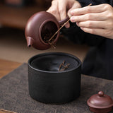 Person pouring tea from a purple teapot into a black ceramic multipurpose ashtray 
