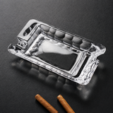 Clear crystal glass cigar ashtray with dual cigar rests on dark tabletop