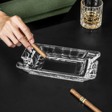 Hand holding a cigar, stubbing cigar on a clear crystal glass cigar ashtray