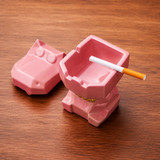 Open pink ceramic hippo ashtray with lid removed and built-in grooves to rest cigarettes on a wooden table