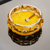 Amber glass ashtray with cigarette on reflective tabletop