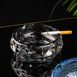 Smoke gray glass ashtray with lit cigarette on black surface