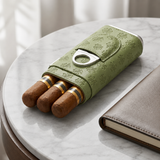 Sage green leather cigar holder with three cigars beside a notebook