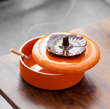 Persimmon ceramic ashtray with lid partly open on wooden table