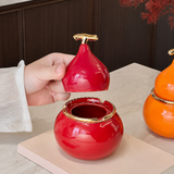Red gourd-shaped ceramic ashtray with removable lid lifted by hand