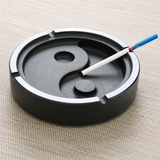Heavy stone yin-yang ashtray with cigarette rests and cigarette on tabletop