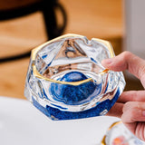 Blue iceberg glass ashtray in hand with gold rim, thick glass body, and modern crystal design