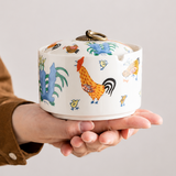 Lidded ceramic ashtray with rooster pattern held in hand to show compact size