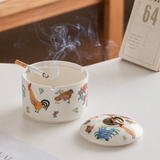 Ceramic ashtray with rooster pattern, cigarette rest grooves, smoke, and matching lid