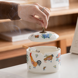 Hand lifting lid from rooster pattern ceramic ashtray with cigarette resting on rim