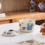 Ceramic rooster ashtray with lid, cigarette, smoke, and drink in cozy tabletop setting