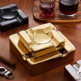 Top angled view of gold square cigar ashtrays on wooden table with drink glasses