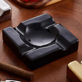Side view of black square ceramic cigar ashtray on wooden table