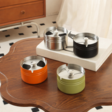 Short and tall stainless steel ashtrays with covered rotating lids on wooden table