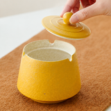 Hand lifting the lid from a mustard yellow textured ceramic ashtray