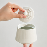 Hand removing the lid from an ivory white covered ceramic ashtray