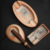 Three rustic ceramic cigar ashtray shapes displayed with cigars on a black tabletop