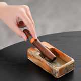 Hand placing a cigar on a rectangular rustic ceramic cigar ashtray