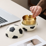 Hand lifting gold removable metal tray from soccer ball covered ashtray