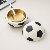 Soccer ball covered ashtray with gold metal tray and cigarette on tabletop