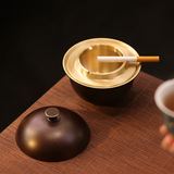 Dark bronze brass ashtray with lid open on tabletop