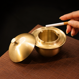 Gold brass ashtray with lid removed and cigarette rests around rim