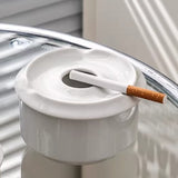White ceramic ashtray with cigarette resting across the top on reflective surface