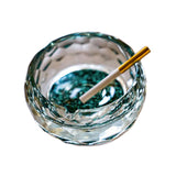 Round crystal glass ashtray with turquoise base and cigarette on white background