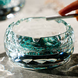 Hand using round glass ashtray with turquoise base on tabletop