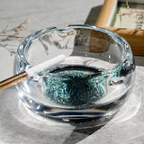 Clear round glass ashtray with turquoise base on tabletop