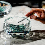 Hand using round glass ashtray with turquoise base on tabletop