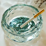 Round crystal glass ashtray with turquoise base and cigarette on bright surface