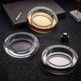 Gold, smoked gray, and clear crystal glass ashtrays on black surface
