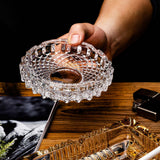 Hand holding clear diamond-pattern glass ashtray above a wooden table