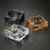 Clear, gray, and amber square glass ashtrays displayed on dark tabletop