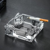 Clear square glass ashtray with cigarette on dark surface