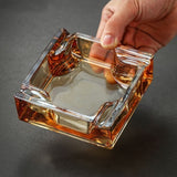 Hand holding amber square glass ashtray