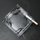 Clear square glass ashtray with cigarette on dark surface