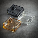 Gray, amber, and clear square glass ashtrays on dark surface