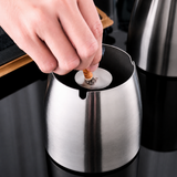 Hand extinguishing a cigarette on the center plate inside a stainless steel ashtray