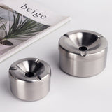 Two silver stainless steel ashtrays with funnel lids on tabletop