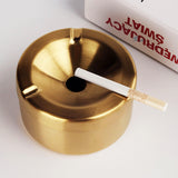 Gold stainless steel ashtray with cigarette resting across the top