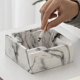 Hand placing cigarette on square marble pattern ashtray with practical edge grooves