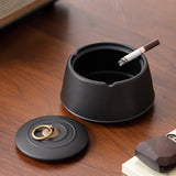 Open black ceramic ashtray with cigarette and removable lid on wooden table