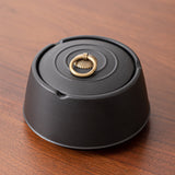 Closed black ceramic ashtray with decorative metal ring on wooden table