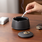 Hand placing a cigarette into an open black ceramic ashtray