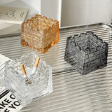 Amber and smoked gray square glass ashtrays on striped surface