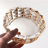 Top view of amber crystal glass ashtray in hand, thick round ashtray with geometric edge design
