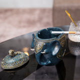Blue elephant resin ashtray with cigarette resting in covered ashtray base