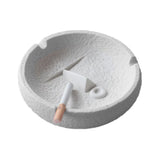 Minimalist face expression ceramic ashtray in white, angled product view with cigarette groove